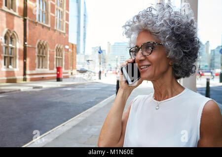 Middle aged woman talking on phone in city street, close up Stock Photo