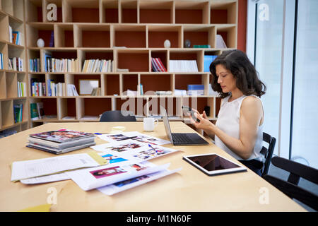 Woman in creative media office using smartphone at her desk Stock Photo