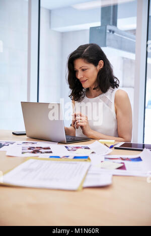 Woman in creative media office using laptop, vertical Stock Photo