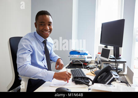 Young black man smiling to camera from his desk in an office Stock Photo