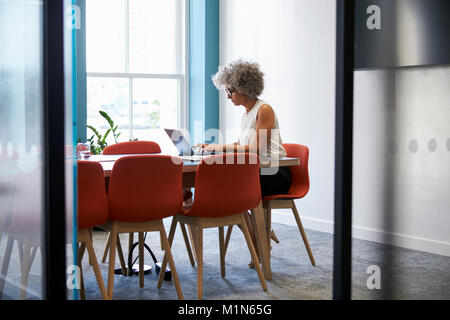 Middle aged woman working alone in office boardroom Stock Photo