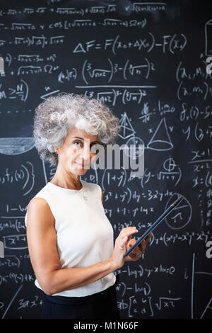 Middle aged academic woman at blackboard smiling to camera Stock Photo