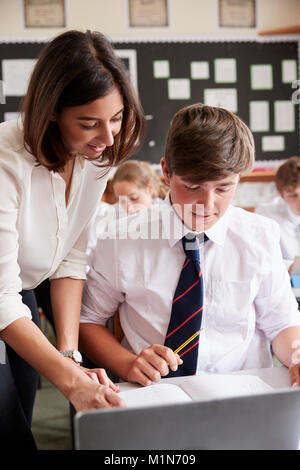 Female Teacher Helping Pupil Using Computer In Classroom Stock Photo