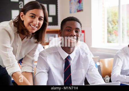 Portrait Of Teacher Helping Pupil Using Computer In Classroom Stock Photo