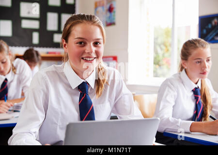 Portrait Of Female Pupil In Uniform Using Laptop In Classroom Stock Photo