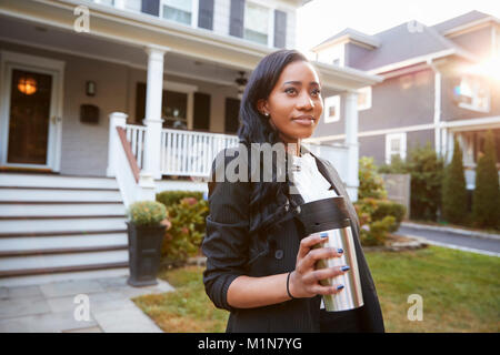 Businesswoman With Cup Of Coffee Leaving Suburban House For Work Stock Photo
