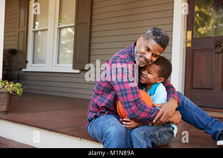 Father And Son Discussing Basketball On Porch Of Home Stock Photo