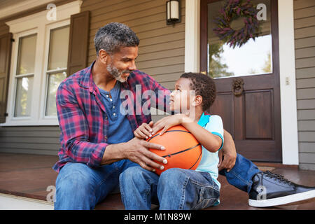 Father And Son Discussing Basketball On Porch Of Home Stock Photo