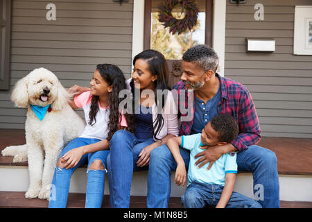 Family With Children And Pet Dog Sit On Steps Of Home Stock Photo