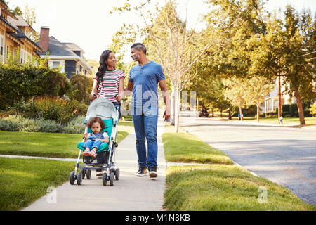 Couple Push Daughter In Stroller As They Walk Along Street Stock Photo