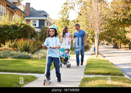 Couple Push Daughter In Stroller As Son Rides Scooter Stock Photo