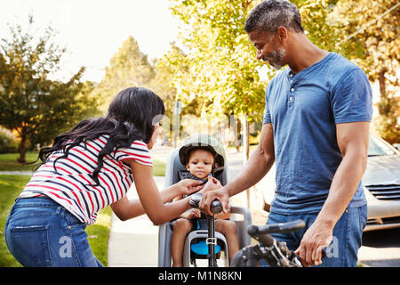 Parents Putting Daughter Into Child Seat For Bike Ride Stock Photo