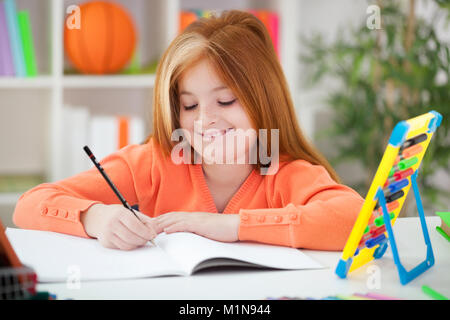 smiling red-haired girl doing her homework at home Stock Photo