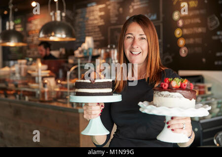Portrait Of Female Owner With Cakes On Stands In Coffee Shop Stock Photo