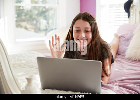 Teen girl lying on bed making a video call with laptop Stock Photo