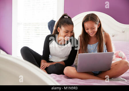 Two teen girls sitting on bed using a laptop, close up Stock Photo