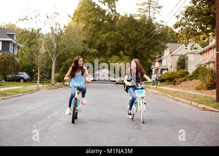Two teen girls riding bikes in a quiet street, front view Stock Photo