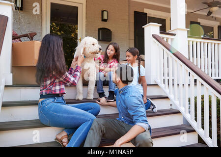 Family With Dog Sitting On Steps Of New Home On Moving In Day Stock Photo