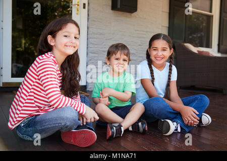 Portrait Of Children Sitting On Porch Of House Together Stock Photo
