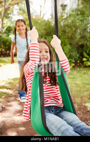 Two Sisters Having Fun On Garden Swing At Home Stock Photo