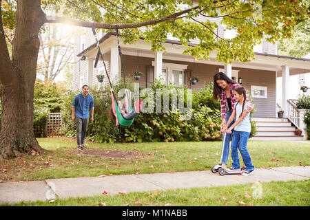 Children Playing On Garden Swing And Scooter Outside House Stock Photo