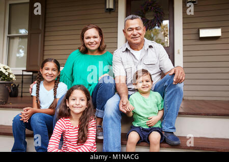 Grandparents With Grandchildren Sit On Steps Leading Up To Home Stock Photo