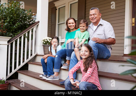 Grandparents With Grandchildren Sit On Steps Leading Up To Home Stock Photo