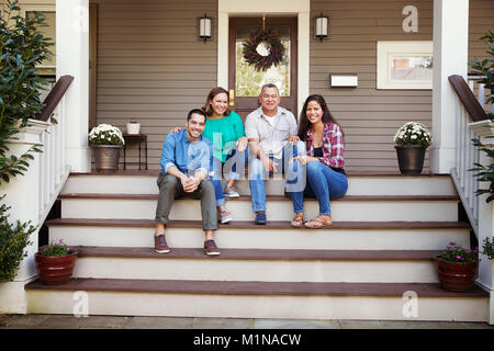 Parents With Adult Offspring Sitting On Steps in Front Of House Stock Photo