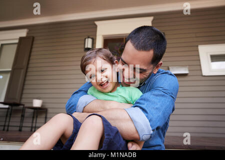 Father Hugging Son As They Sit On Porch Of House Together Stock Photo