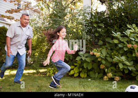 Grandfather Playing Soccer In Garden With Granddaughter Stock Photo