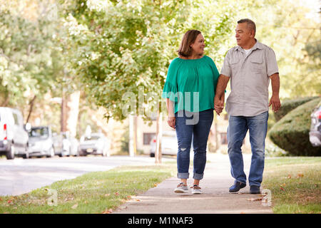 Senior Couple Walking Along Suburban Street Holding Hands Stock Photo