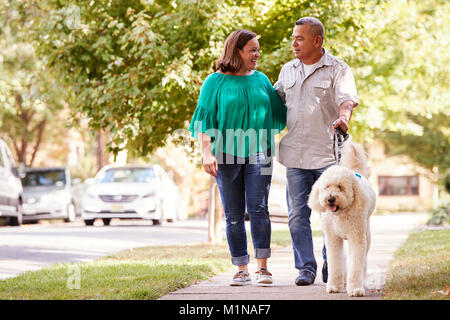 Senior Couple Walking Dog Along Suburban Street Stock Photo