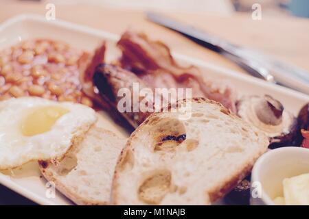 Cooked breakfast with toast, bacon, fried egg, sausage, baked beans, mushroom and butter - filter applied Stock Photo