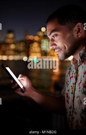 Man Using Mobile Phone At Night With City Skyline In Background Stock Photo