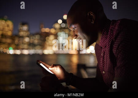 Man Using Mobile Phone At Night With City Skyline In Background Stock Photo