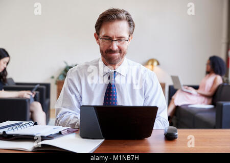 Businessman using laptop at desk, colleagues in background Stock Photo