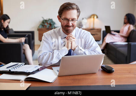 Businessman using laptop at desk, colleagues in background Stock Photo