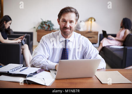 Businessman using laptop at desk smiling to camera Stock Photo
