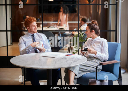 Male and female colleagues talk over coffee at office cafe Stock Photo