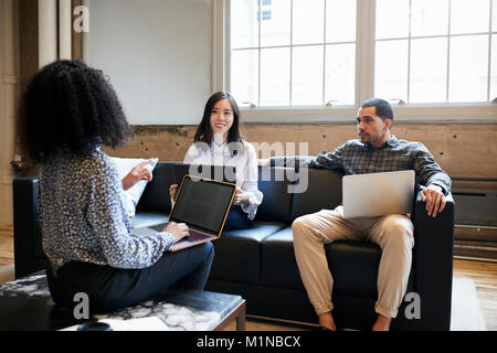 Three young colleagues with laptops at a casual work meeting Stock Photo