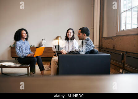 Smiling work colleagues using laptops at a casual meeting Stock Photo