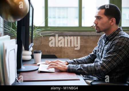 Hispanic man working at a computer in an office, side view Stock Photo