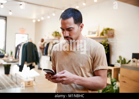 Young Hispanic man using smartphone in a clothes shop Stock Photo
