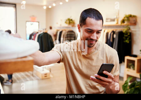 Smiling Hispanic man using smartphone in a clothes shop Stock Photo