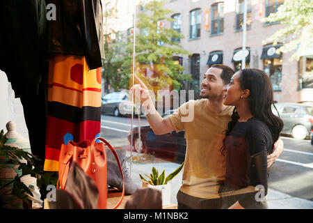 Smiling couple pointing at clothes in a shop window Stock Photo