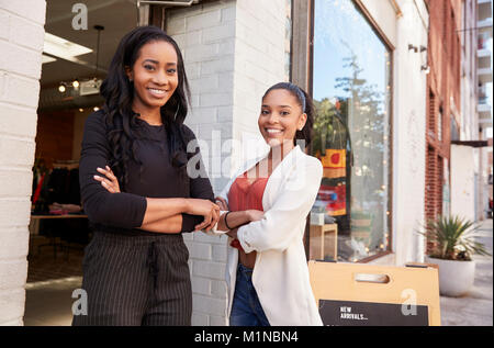 Two young women smiling to camera outside their clothes shop Stock Photo