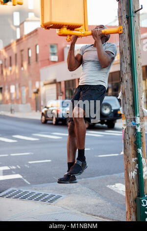 Young black man doing chin ups in Brooklyn street, vertical Stock Photo