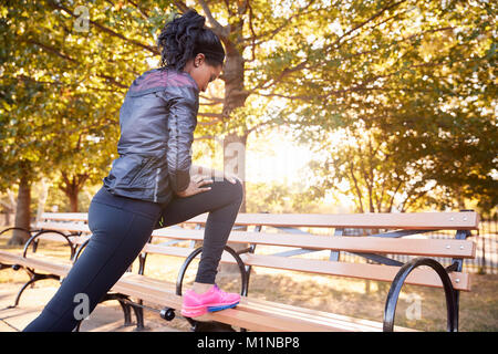 Young black woman stretching on a bench in a Brooklyn park Stock Photo
