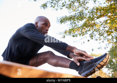Young black man stretching leg on a bench in park, close up Stock Photo