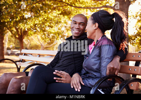 Young black couple sitting on bench in Brooklyn park Stock Photo